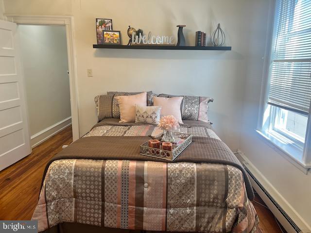 bedroom with wood-type flooring and a baseboard heating unit