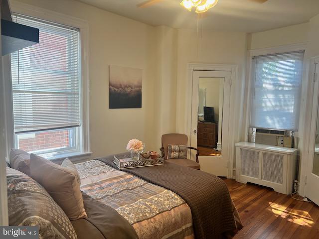 bedroom with dark wood-type flooring, radiator heating unit, and multiple windows