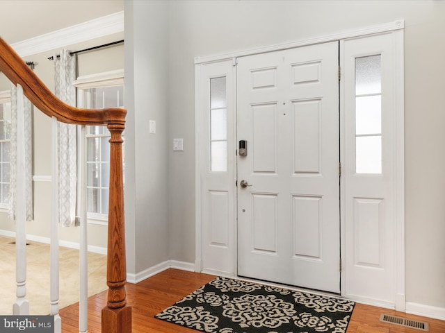 entryway with ornamental molding, wood finished floors, visible vents, and baseboards