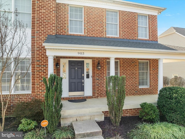 entrance to property featuring brick siding, a porch, and a shingled roof