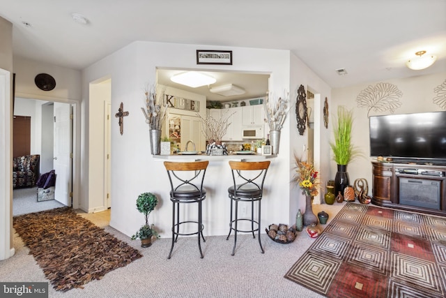 kitchen featuring white cabinetry, light colored carpet, kitchen peninsula, and a kitchen bar