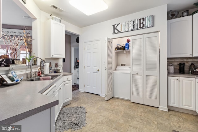 kitchen featuring dishwasher, washer / dryer, sink, white cabinets, and backsplash