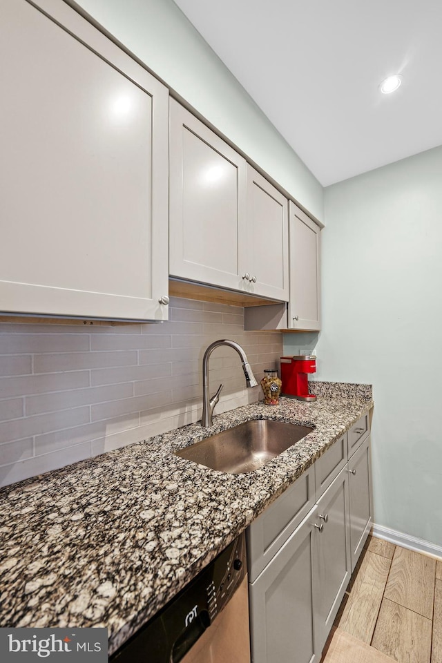 kitchen with sink, light hardwood / wood-style flooring, decorative backsplash, stainless steel dishwasher, and dark stone counters