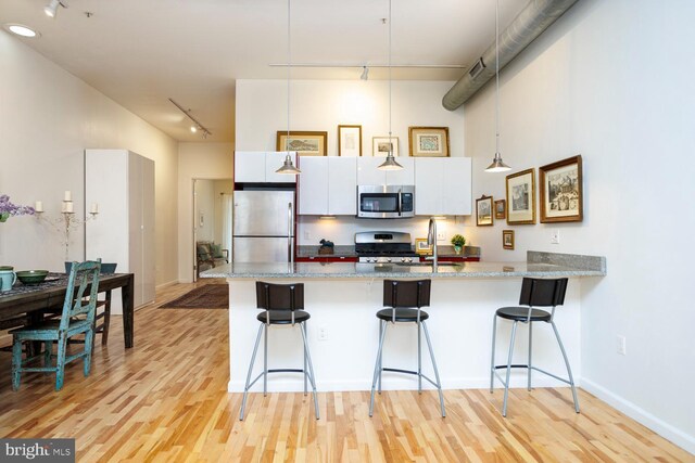 1215 N Hancock St, Philadelphia, PA 19122 - kitchen featuring white cabinetry, stainless steel appliances, a high ceiling, light stone countertops, and a kitchen bar