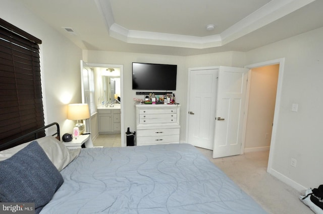 carpeted bedroom featuring a tray ceiling and ensuite bathroom