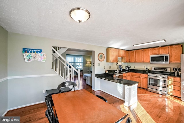 kitchen with light hardwood / wood-style flooring, kitchen peninsula, and appliances with stainless steel finishes