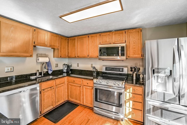 kitchen featuring sink, a textured ceiling, appliances with stainless steel finishes, dark stone counters, and light hardwood / wood-style floors