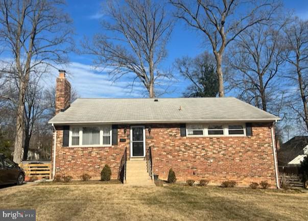 ranch-style house featuring a chimney, a front lawn, and brick siding