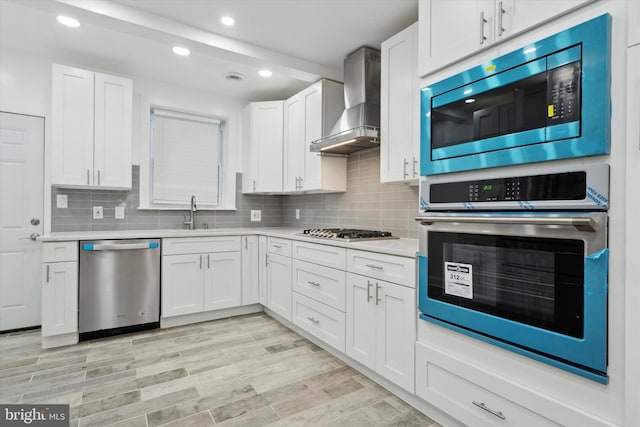 kitchen with sink, appliances with stainless steel finishes, wall chimney range hood, decorative backsplash, and white cabinets