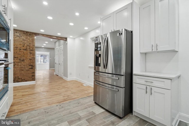 kitchen with light stone countertops, stainless steel refrigerator with ice dispenser, brick wall, and white cabinets