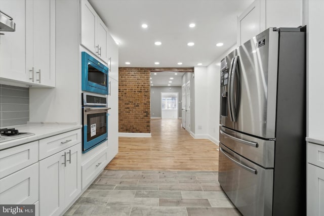 kitchen with brick wall, light stone countertops, white cabinets, and appliances with stainless steel finishes