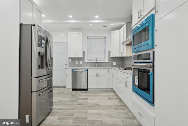 kitchen with appliances with stainless steel finishes, sink, white cabinets, decorative backsplash, and light hardwood / wood-style floors