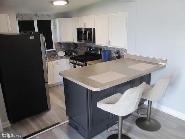 348 Broad St, Mount Holly, NJ 08060 - kitchen featuring appliances with stainless steel finishes, a peninsula, backsplash, white cabinets, and light wood-style flooring