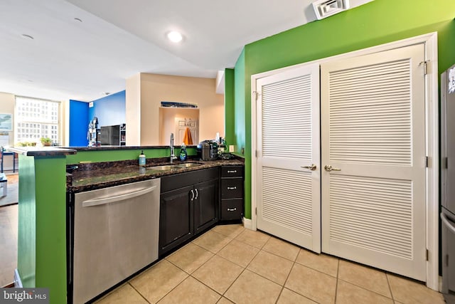 kitchen featuring a sink, dark stone countertops, stainless steel dishwasher, a peninsula, and light tile patterned floors