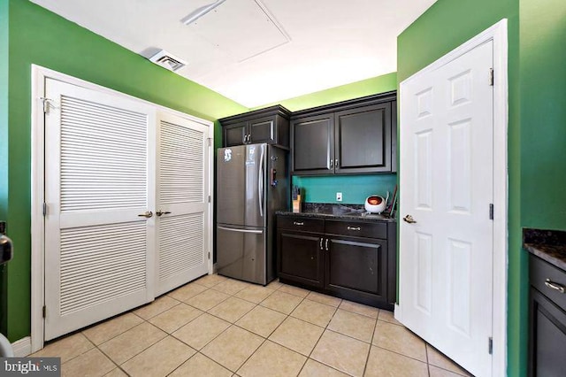 kitchen with light tile patterned flooring, visible vents, dark stone countertops, and freestanding refrigerator