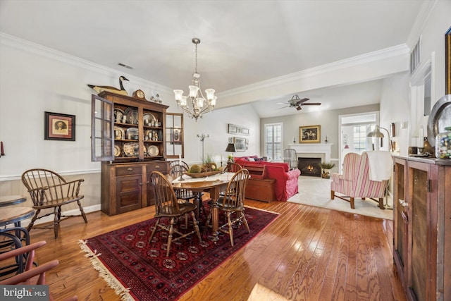 dining room with ornamental molding, wood-type flooring, and ceiling fan with notable chandelier