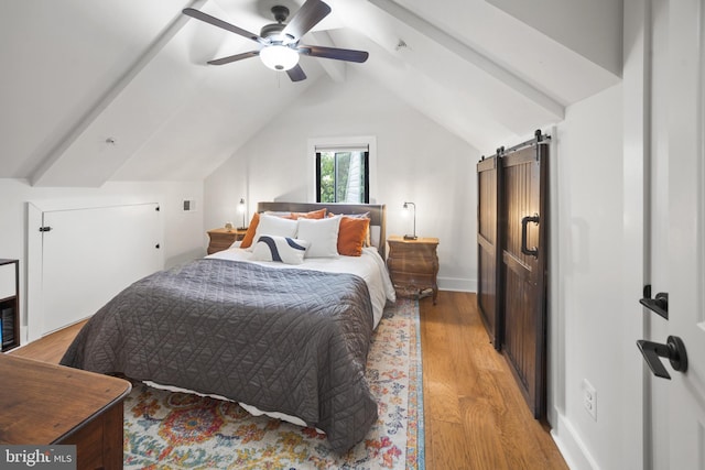 bedroom featuring light hardwood / wood-style flooring, lofted ceiling with beams, a barn door, and ceiling fan