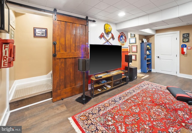 living room featuring a barn door, dark hardwood / wood-style flooring, and a drop ceiling