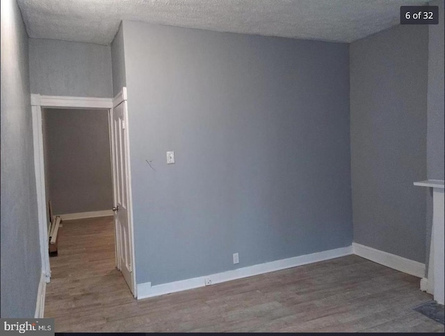 empty room with hardwood / wood-style flooring, a textured ceiling, and baseboard heating