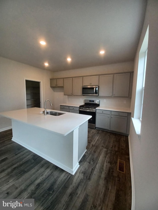 kitchen with sink, gray cabinetry, dark hardwood / wood-style flooring, a kitchen island with sink, and stainless steel appliances