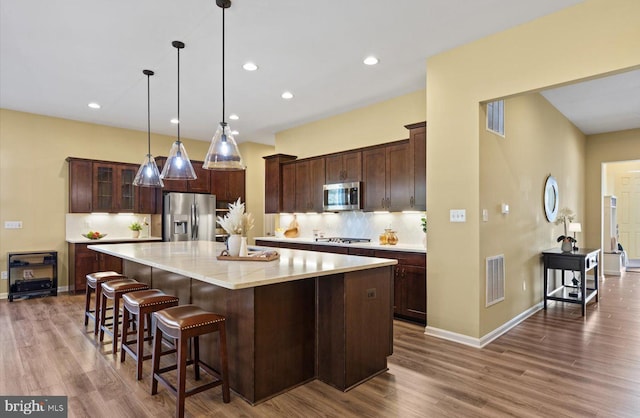 kitchen featuring hanging light fixtures, dark brown cabinets, stainless steel appliances, a spacious island, and tasteful backsplash