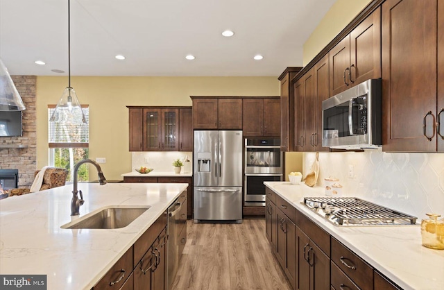 kitchen featuring sink, stainless steel appliances, hanging light fixtures, and light stone countertops