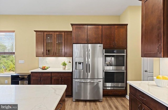 kitchen featuring tasteful backsplash, light wood-type flooring, light stone countertops, and appliances with stainless steel finishes