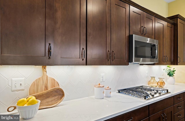 kitchen featuring dark brown cabinetry, stainless steel appliances, light stone countertops, and backsplash