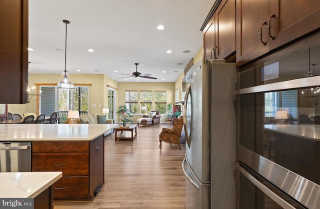 kitchen featuring ceiling fan, appliances with stainless steel finishes, hanging light fixtures, and light wood-type flooring