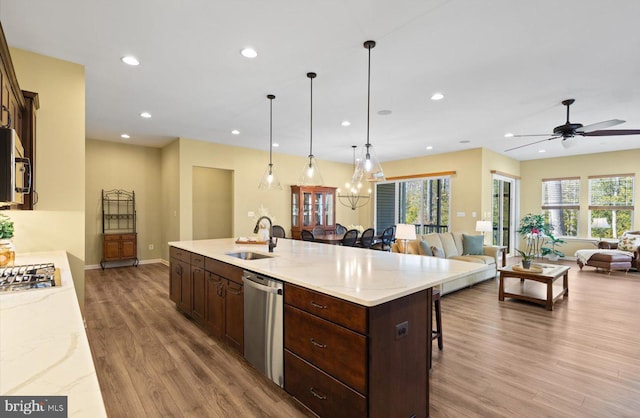 kitchen with sink, dark brown cabinets, hanging light fixtures, a center island with sink, and appliances with stainless steel finishes