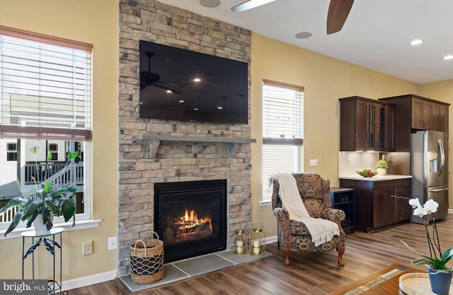 living room featuring a stone fireplace, light hardwood / wood-style flooring, and ceiling fan