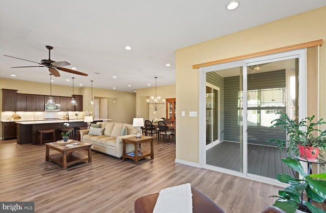 living room with ceiling fan with notable chandelier and light hardwood / wood-style floors