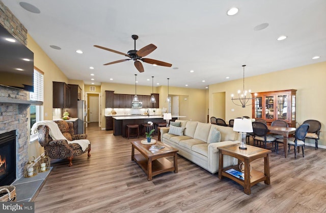 living room featuring a stone fireplace, ceiling fan with notable chandelier, and light wood-type flooring