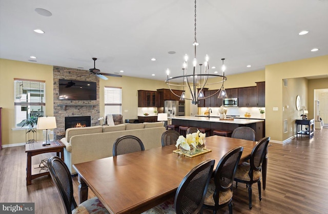 dining space with dark wood-type flooring, sink, a fireplace, and ceiling fan with notable chandelier