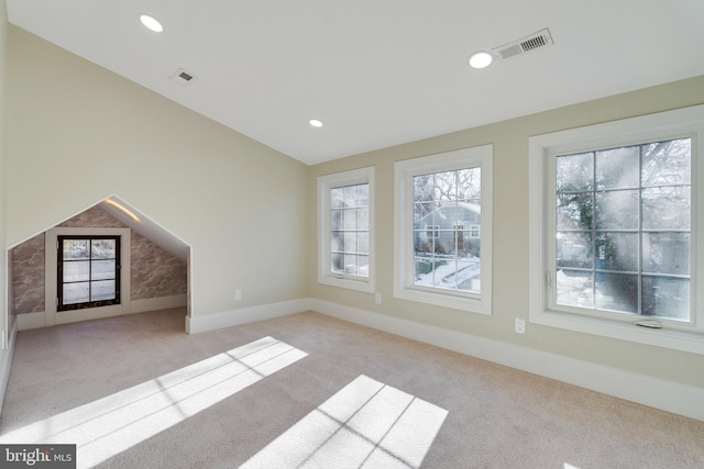 unfurnished living room featuring lofted ceiling, a healthy amount of sunlight, and light colored carpet