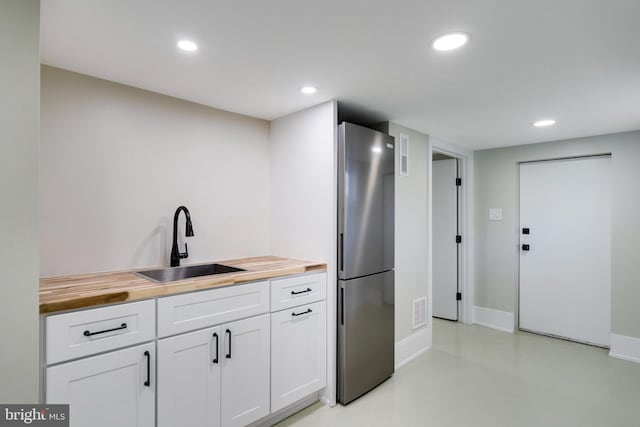 kitchen with sink, stainless steel fridge, butcher block countertops, and white cabinets