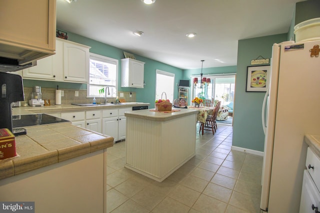 kitchen with hanging light fixtures, tile counters, a kitchen island, white fridge, and white cabinets
