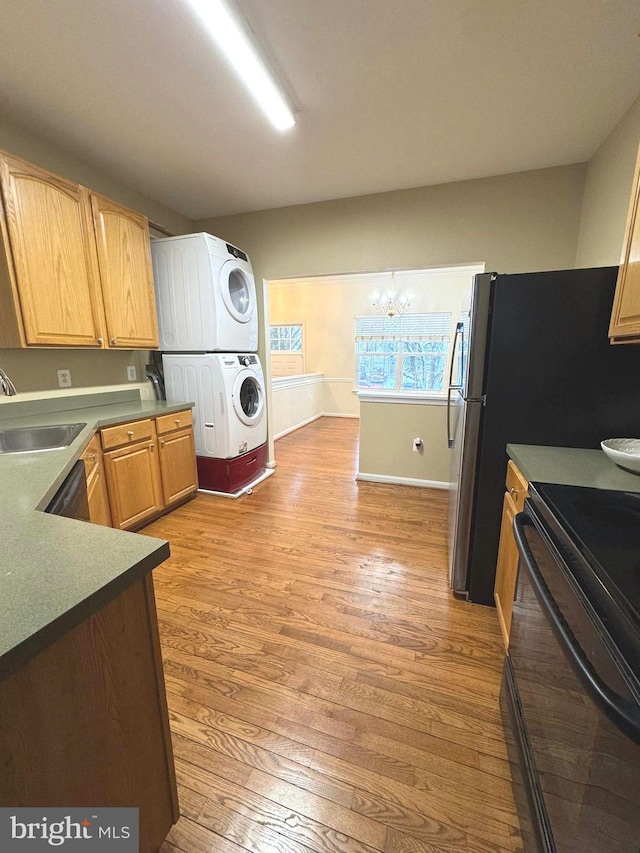 kitchen with sink, an inviting chandelier, stacked washer / drying machine, light hardwood / wood-style floors, and black range with electric cooktop