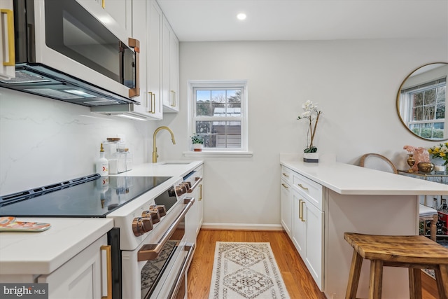 kitchen featuring range with electric stovetop, a sink, white cabinets, stainless steel microwave, and a kitchen bar