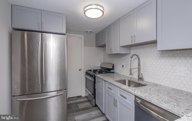 kitchen featuring dark wood-style flooring, a sink, appliances with stainless steel finishes, light stone countertops, and tasteful backsplash