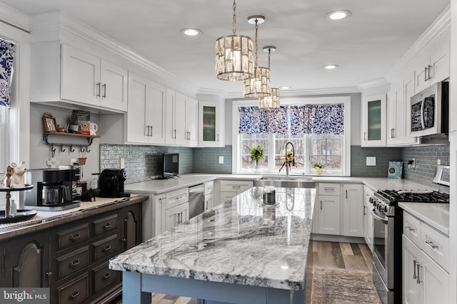 kitchen featuring a kitchen island, white cabinetry, sink, ornamental molding, and stainless steel appliances