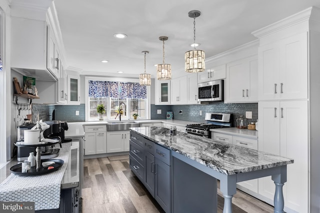 kitchen featuring a kitchen island, appliances with stainless steel finishes, pendant lighting, white cabinetry, and sink