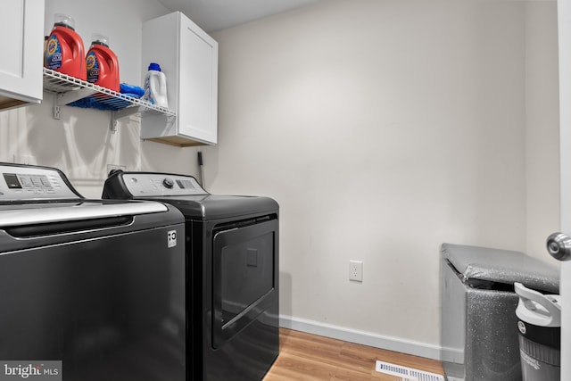 clothes washing area featuring cabinets, separate washer and dryer, and light wood-type flooring