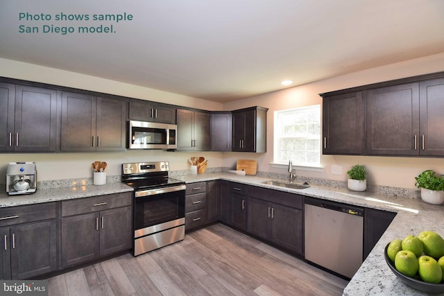 kitchen with dark brown cabinetry, a sink, light wood-style floors, appliances with stainless steel finishes, and light stone countertops