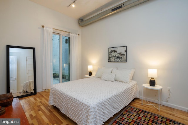 bedroom featuring rail lighting, hardwood / wood-style floors, and access to exterior