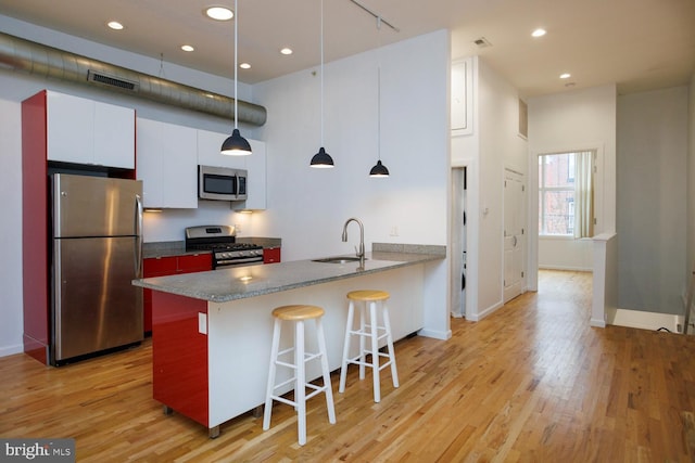 kitchen with appliances with stainless steel finishes, sink, white cabinets, a kitchen bar, and light hardwood / wood-style flooring