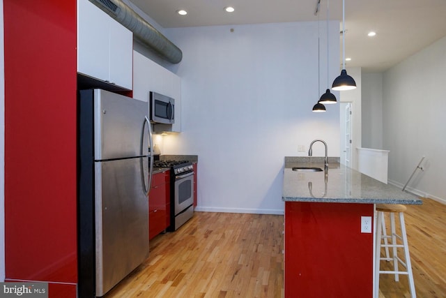 kitchen featuring sink, a breakfast bar area, white cabinetry, decorative light fixtures, and stainless steel appliances