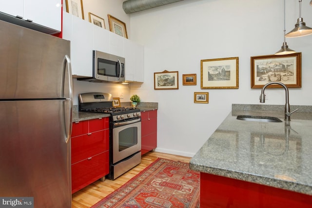 kitchen with sink, pendant lighting, stainless steel appliances, light hardwood / wood-style floors, and white cabinets