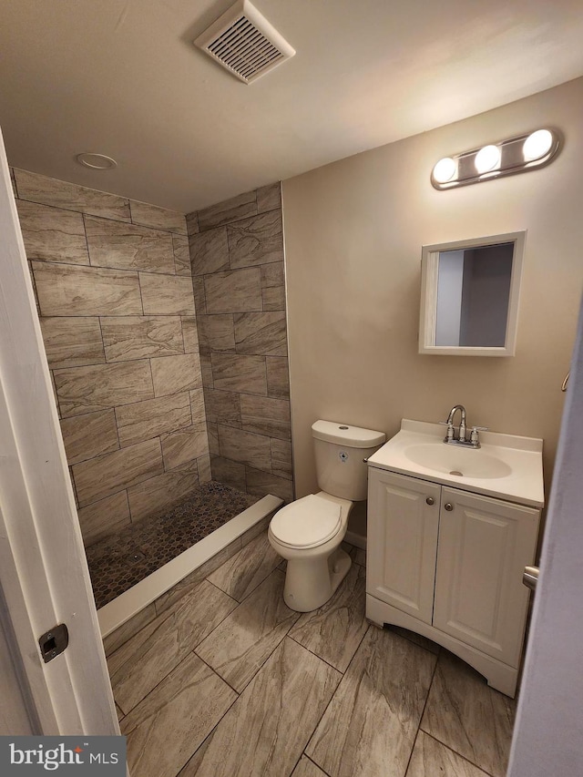 bathroom with a tile shower, vanity, and toilet