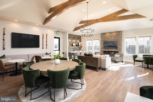 dining space featuring beam ceiling, high vaulted ceiling, a notable chandelier, a fireplace, and light wood-type flooring